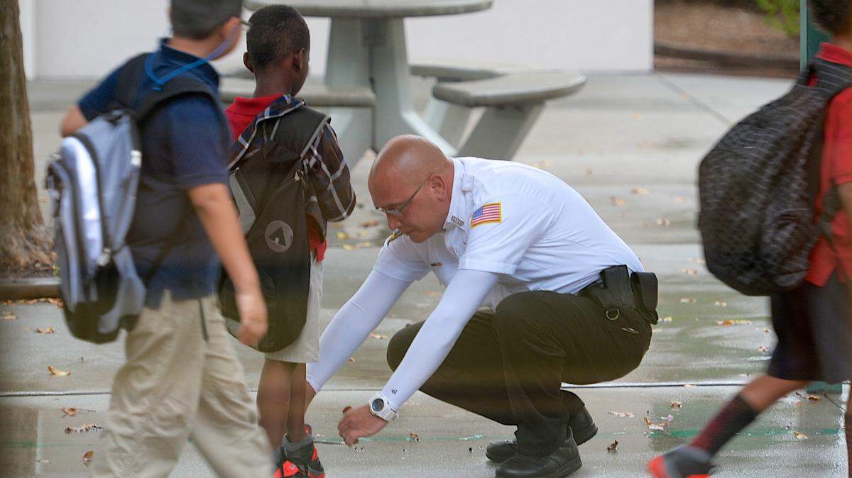 School security guard Frank Uzzolino pauses to help tie the shoelaces of a student at Oneco Elementary in Bradenton as children head to their classes.HERALD FILE PHOTO/PAUL VIDELA