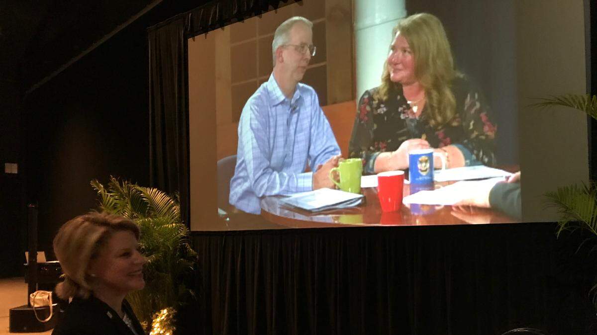 Jacki Dezelski, president and CEO of the Manatee Chamber of Commerce, stands in front of a super-sized video screen showing a discussion between outgoing chairman of the board Darcie Duncan and incoming chairman Bill Poulton on Thursday night at the Bradenton Area Convention Center.