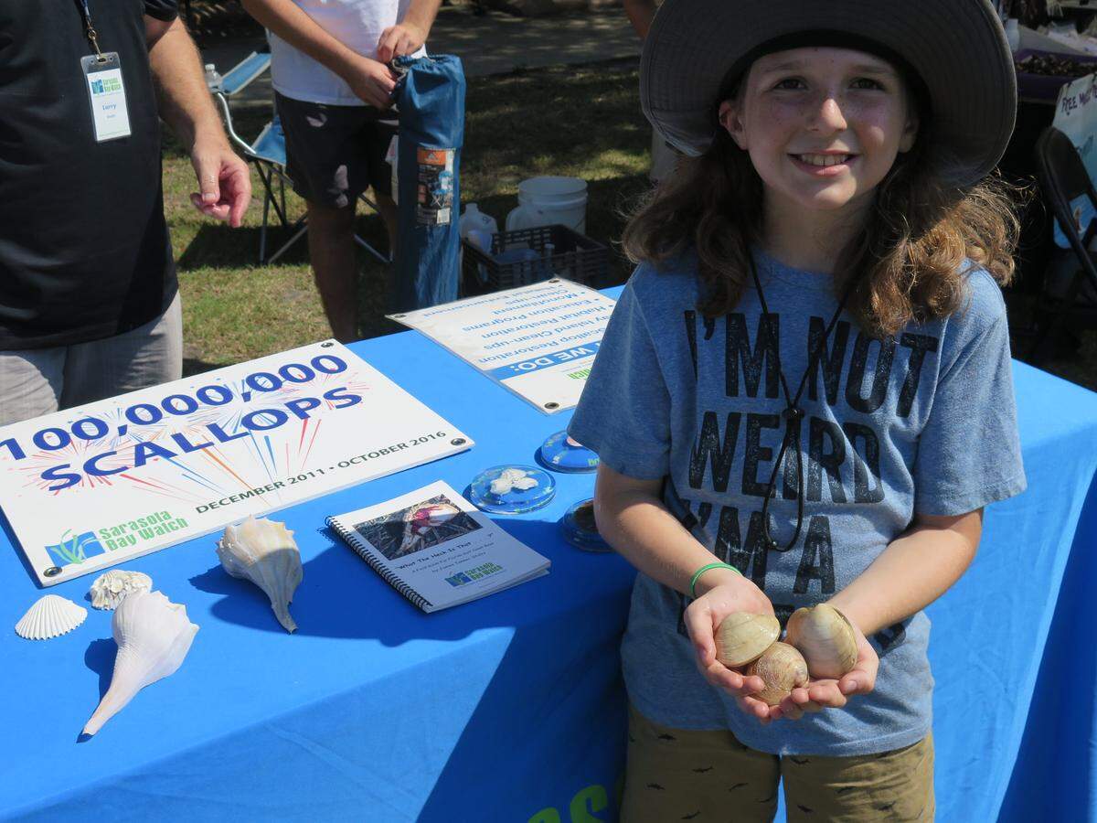 Lawton Roberts poses for a photo at the Sarasota Bay Watch table Saturday afternoon. Volunteers at the booth allowed visitors to interact with clams in a tank.