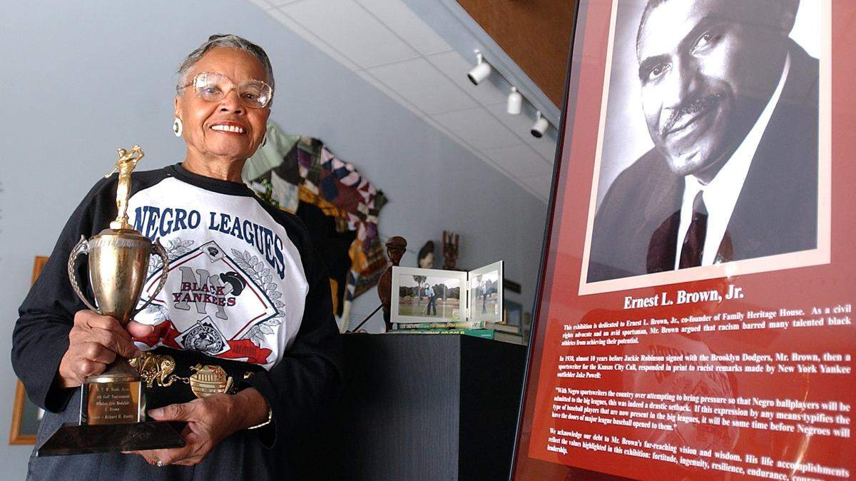 5/9/2002--Fredi Brown holds one of her late husband’s, Ernest Brown, Jr., golf trophies that is on display next to his portrait that welcomes visitors to the Family Heritage House Museum at Manatee Community College. The display is part of the “From Obscurity To Excellence” an exhibit celebrating black achievement in sports.