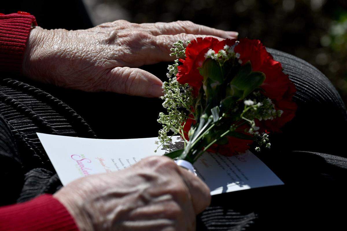 Eleanor Craig, 79 clutches a small bouquet of flowers as she waits in a folding chair to marry Norman Rondeau, 80, in a wedding celebration beside the Historic Manatee County Courthouse on Feb. 14, 2024.
