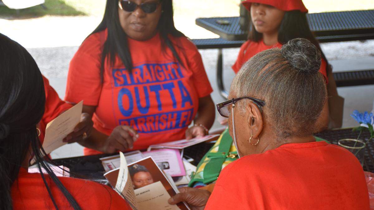 Daisy Cooper, 77, (right) shows off her collection of obituaries and funeral programs that have been preserved over the years to younger generations at the Parrish Community Reunion at Ola Mae Sims Park on Saturday.
