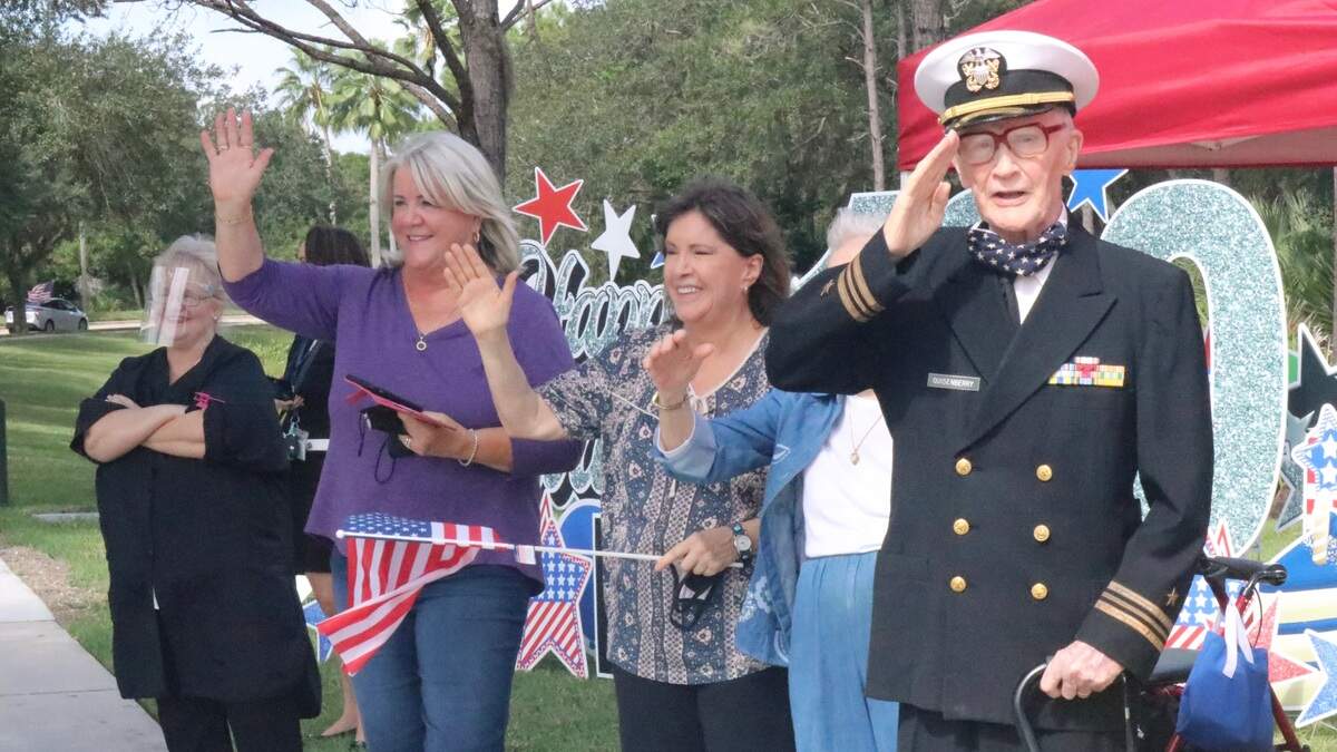 Retired Navy Lt. Cmdr. Roger Quisenberry, a World War II veteran, salutes a drive-by parade that celebrated his 100th birthday. Joining him on Wednesday were wife Peg and daughters Jan Wright and Joy Bragg, shown above.