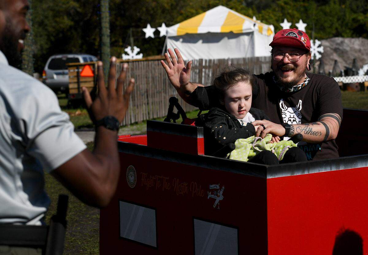 12/08/21—A dad waves to a deputy as he and his child ride a small train after a ride on the North Pole Express from the Florida Railway Museum for a trip to meet Santa at the 36th annual event for terminally ill children.