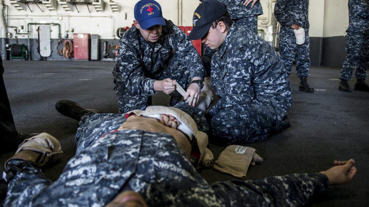Hospital Corpsman 2nd Class Robert Jones, left, from Bradenton, trains Seaman Juan Miranda, from Reading, Pa., on how to apply a splint to a simulated compound fracture during a general quarters drill in the hangar bay of the U.S. Navy's only forward-deployed aircraft carrier USS Ronald Reagan. 
 U.S. Navy photo by Mass Communication Specialist 3rd Class Ryan McFarlane/Released)