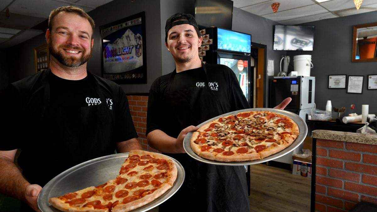 Godson’s owner Philip Chaltis and manager Ashton Hanes hold up fresh pizzas. Godson’s Pizzeria at 3306 Manatee Ave. West serves pizza, wings, subs and more.