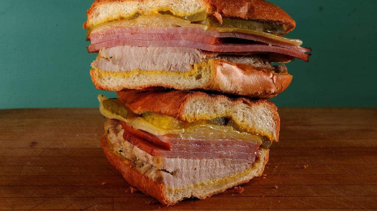 A traditional Cuban sandwich recipe calls for sliced ham, roast pork with a citrusy marinade (called mojo) and Swiss cheese layered in a loaf of Cuban bread. The sandwich is then garnished with pickles and mustard.