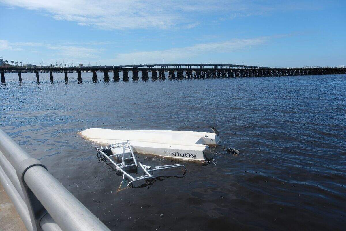 An overturned boat barely breaks the surface of the water by the Bradenton Riverwalk in Manatee County, Fl., after the damage from Hurricane Milton, Thursday, Oct. 10, 2024.