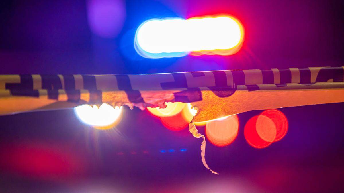A defocused police car sits behind crime scene tape with flashing lights at night.