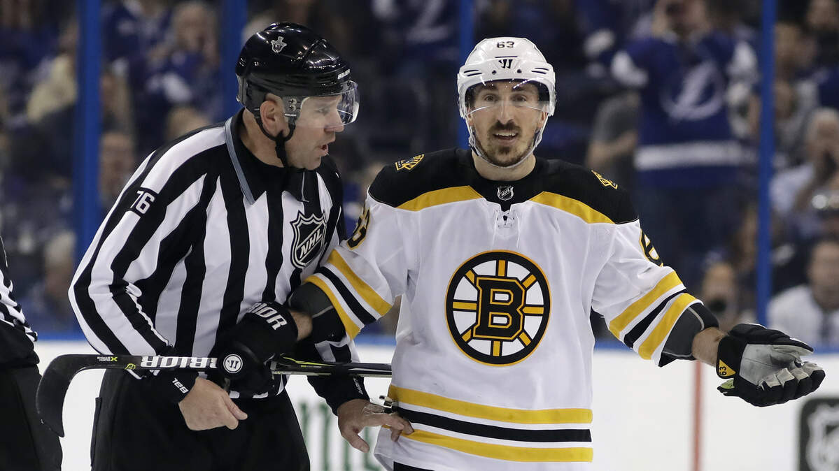Boston Bruins left wing Brad Marchand (63) is escorted off the ice by linesman Michel Cormier (76) after taking a penalty against the Tampa Bay Lightning during the first period of Game 5 of an NHL second-round hockey playoff series Sunday, May 6, 2018, in Tampa, Fla.