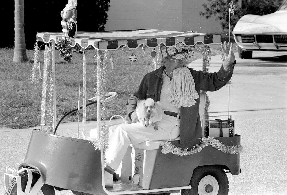 A security cart driver dressed as Santa Claus drives his decorated cart with his poodle-elf by his side. 1980