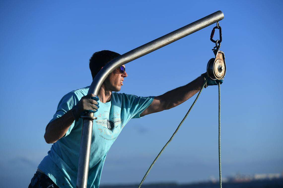 12/15/21—Ryan Brown guides a rope used in a mechanical pulley to haul in nets filled with clams. The seedling clams are set into the shallow waters and pulled up months later when they’re ready.