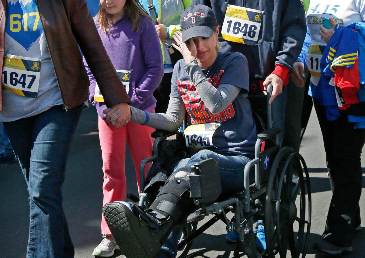 In this April 19, 2014, file photo, Boston Marathon bombings survivor Rebekah Gregory DiMartino wipes tears as she is led in her wheelchair after crossing the finish line of the Boston Marathon Tribute Run in Boston.