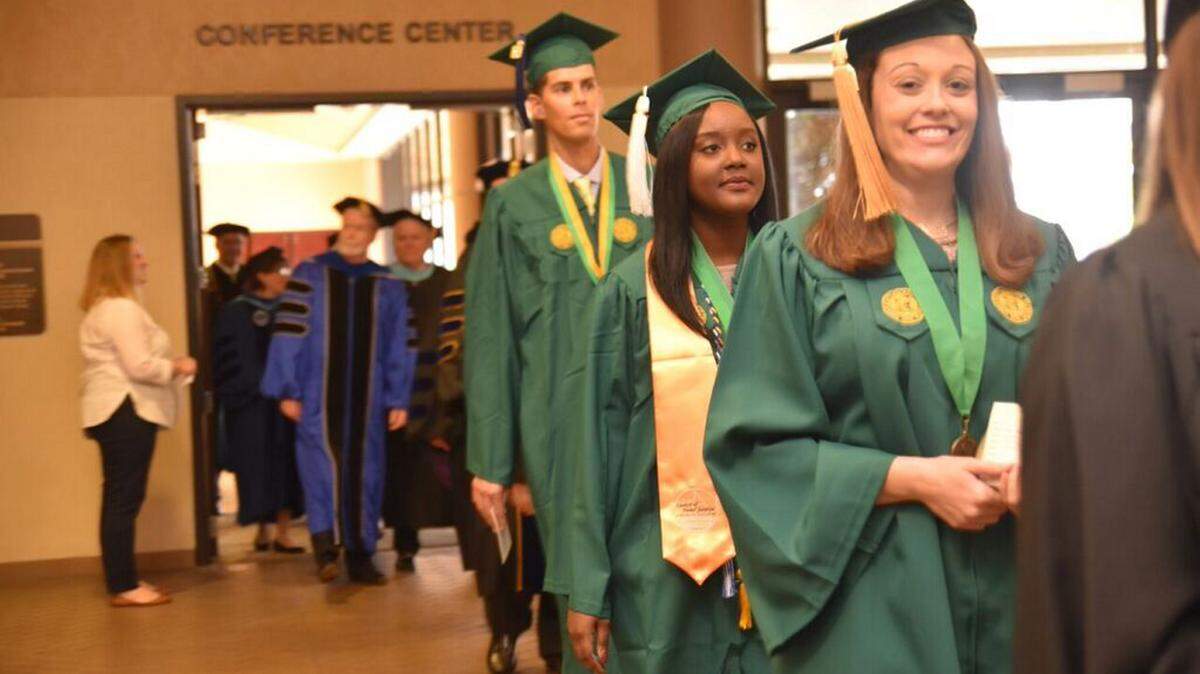 From left to right in green gowns, the University of South Florida Sarasota-Manatee's three student award winners, Matthew Bertrand, Ashley Metelus and Amber Haller begin to walk into the fall commencement at the Bradenton Area Convention Center in Palmetto Sunday. 
 SPECIAL TO THE HERALD/Krista Schrock