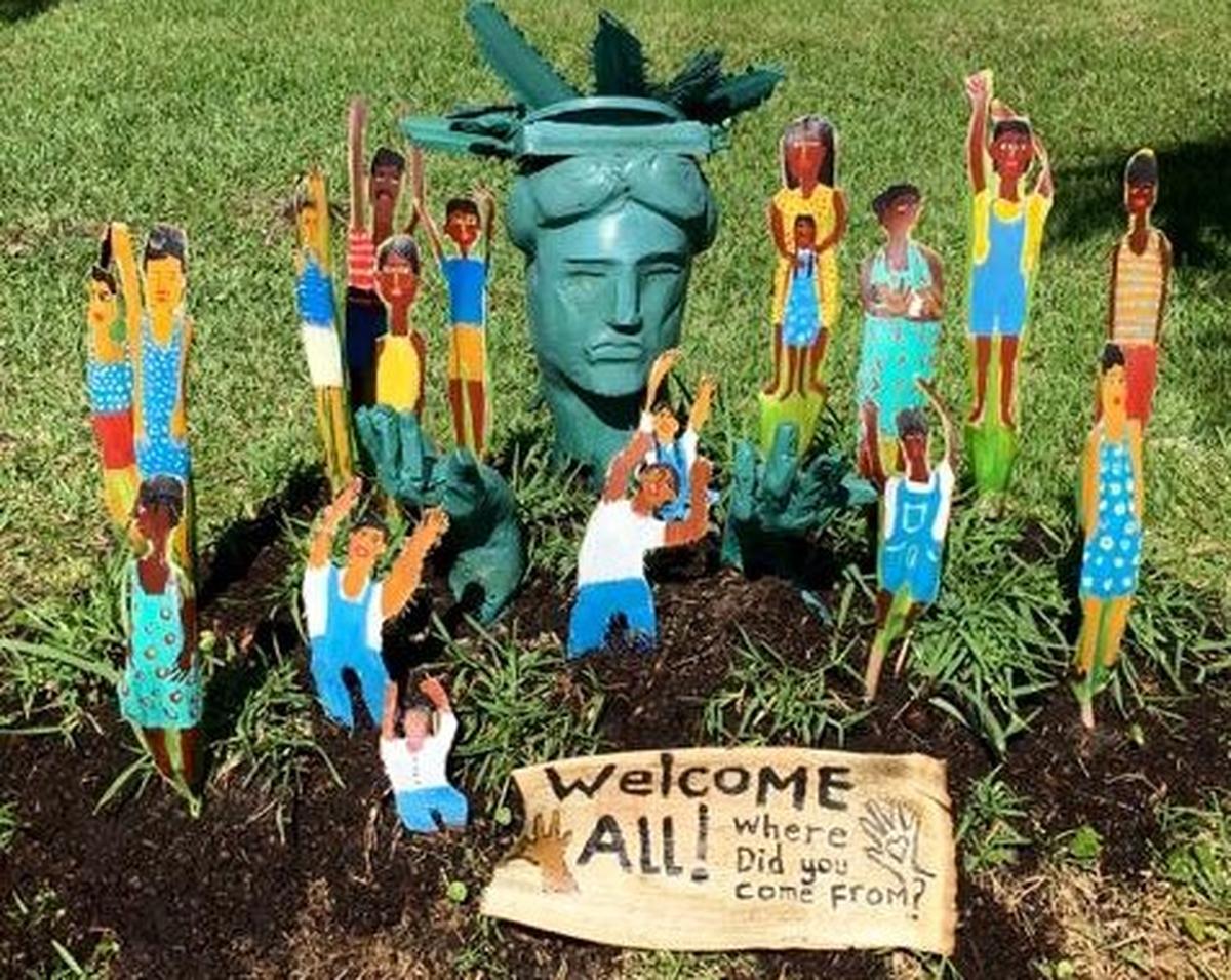 People crafted from palm fronds spring up around a depiction of the Statue of Liberty in one of the latest installations in artist Susan Curry’s front yard in Cortez. A sign reads: “Welcome All! Where did you come from?”