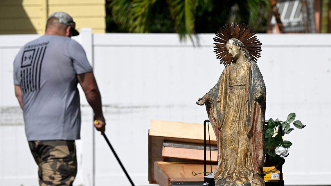 A small statue dries in the sun as a man cleans mud from a deck with the high water mark visible on the fence in Cortez Village in the aftermath of Hurricane Helene in Manatee County on Friday, Sept. 27, 2024.