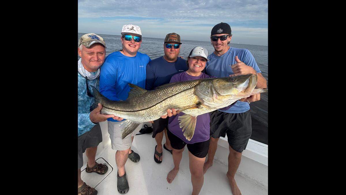 Anglers Chuck Holbrook, Logan Houston, Nico Ferry, Rebecca Ferry and Mike Joyce showcase a large snook that fishing Captain Griffin Deans swam in the water to catch.