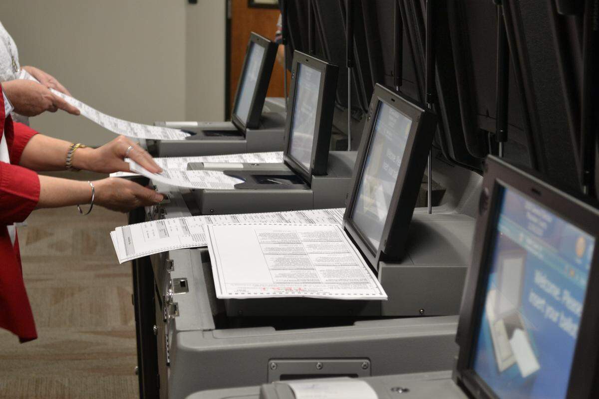 Manatee County Supervisor of Elections employees feed test ballots into voting machines during logic and accuracy training.