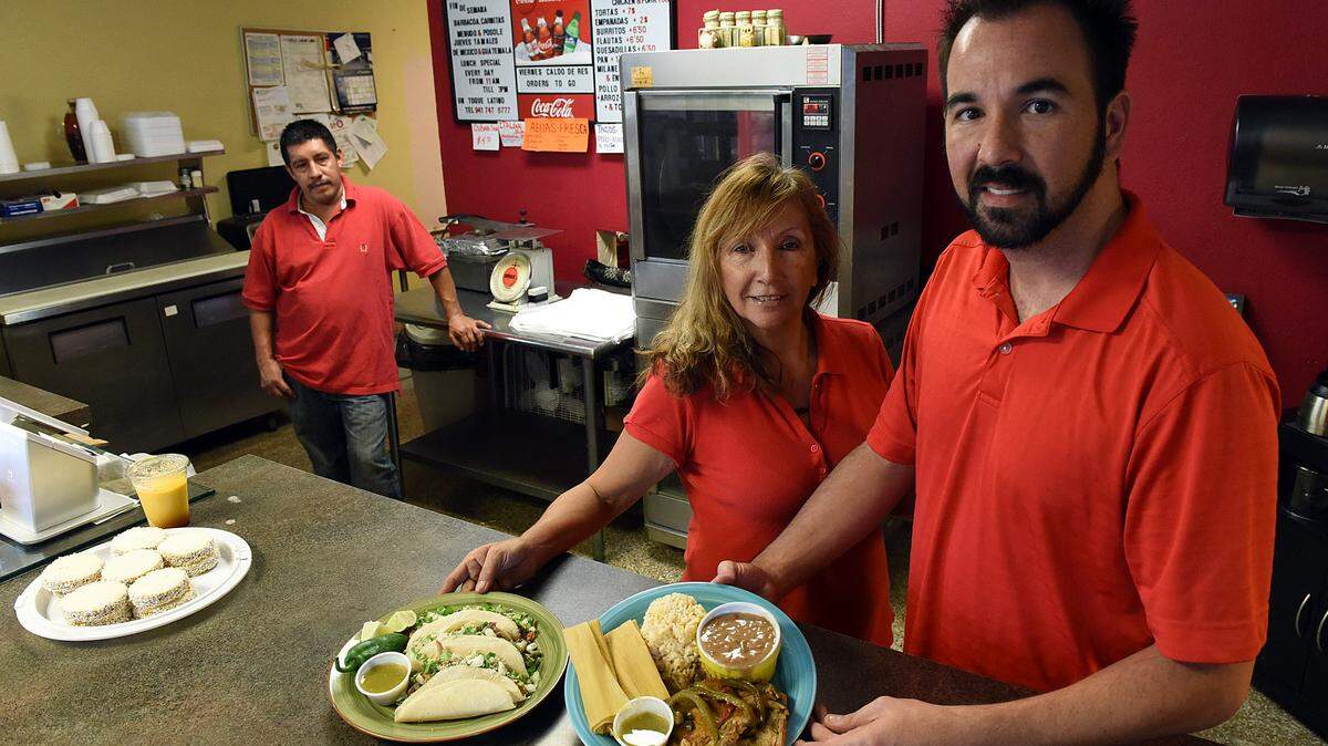 Un Toque Latino co-owners Susana Guerin-Barberana and her son, Wiliam Ballesteros-Guerin, with cook, Abundio Robledo, back left, with plates of tacos and pork chops with tamales, rice and beans. 
 TIFFANY TOMPKINS-CONDIE/Bradenton Herald