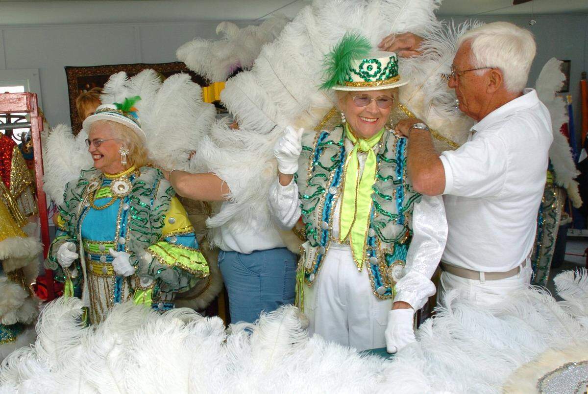03/15/2006 -- Bob Heisse, right, helps strutter Deloris White into her feathered Irish costumery while the Suncoast Mummers String Band performs just outside Wednesday during a Heritage Days event at Braden Castle Park along the Manatee River. At left is Audrey Miller.