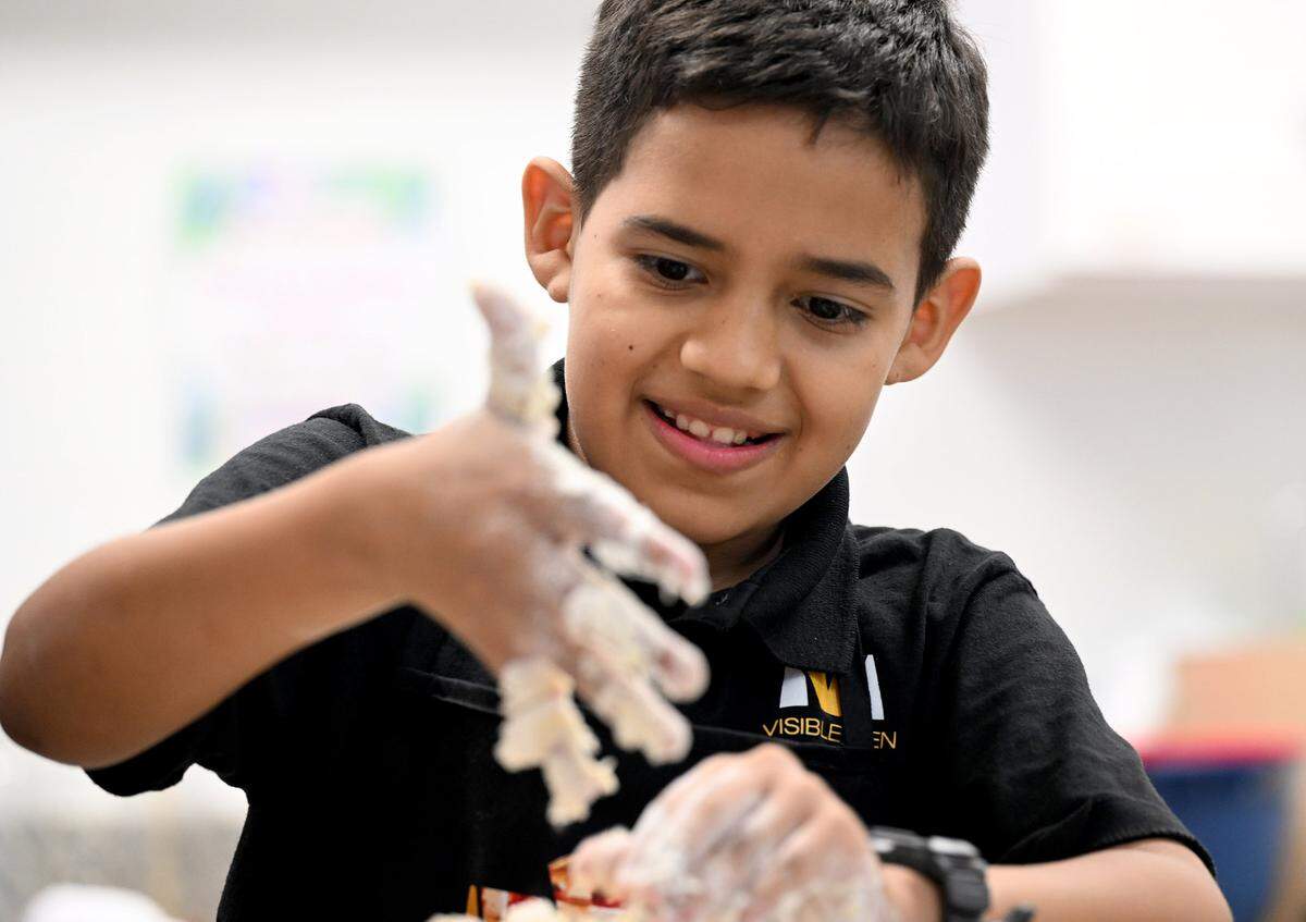 Melkis Ruiz, a 5th-grade student, tries to get sticky pie crust dough off his hands while learning how to make apple pies for Thanksgiving from celebrity chef Marvin Woods.