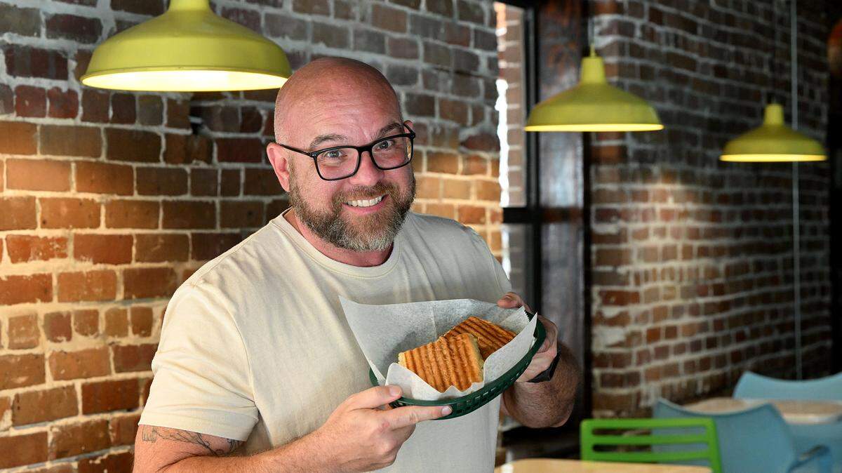 The Brown Bag owner Joey Bennett holds a pressed Cuban sandwich on Old Main Street in downtown Bradenton on May 28, 2025.