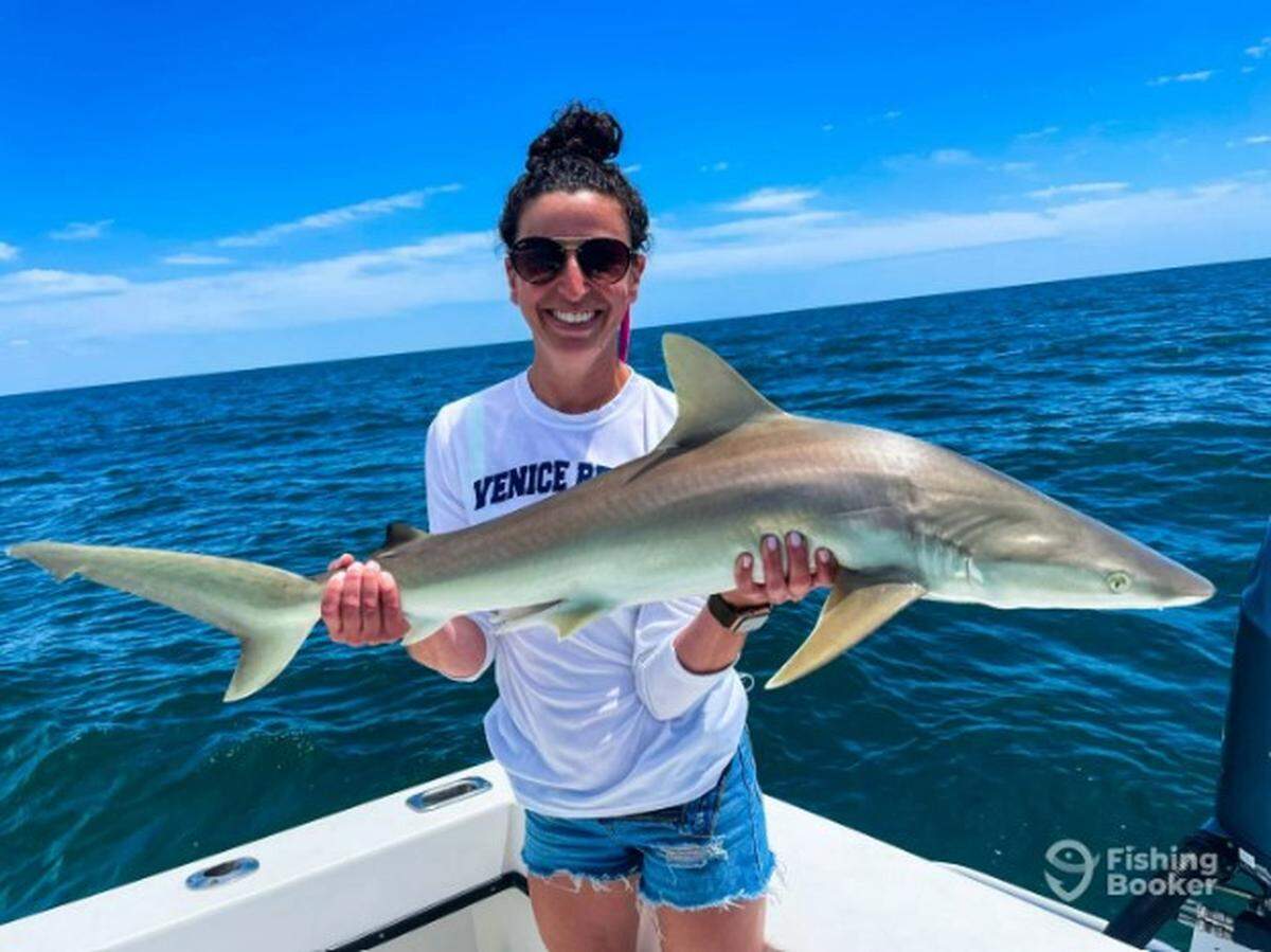 Una mujer sosteniendo un tiburón narigudo que capturó durante una excursión de pesca con el capitán Tony Zain de Skyway Sportfishing, un servicio de alquiler de barcos en Anna Maria Island. Zain es uno de los seis pescadores de barcos de alquiler galardonados con Angler's Choice Award 2022. FishingBooker.com