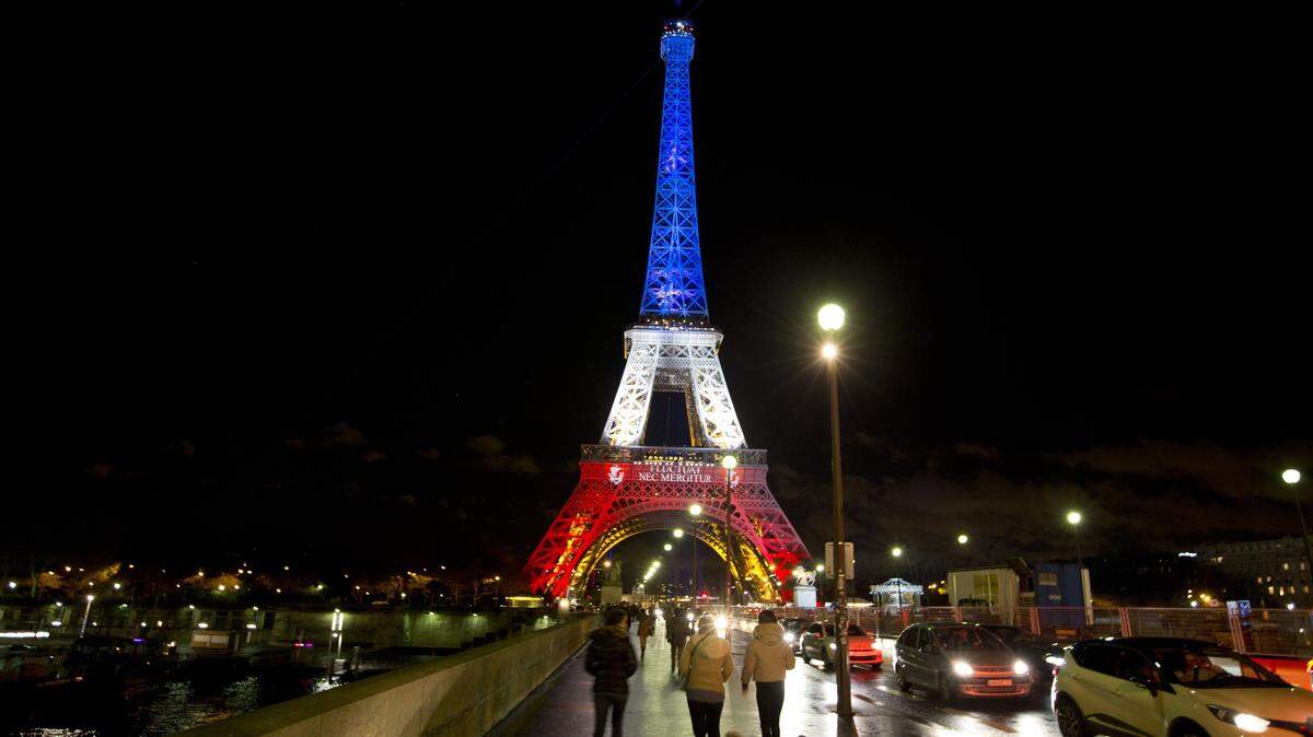 People walk towards the illuminated Eiffel Tower in the French national colors red, white and blue in honor of the victims of the attacks last Friday in Paris, Tuesday, Nov. 17, 2015. France is demanding security aid and assistance from the European Union in the wake of the Paris attacks and has triggered a never-before-used article in the EU's treaties to secure it. (AP Photo/Peter Dejong)