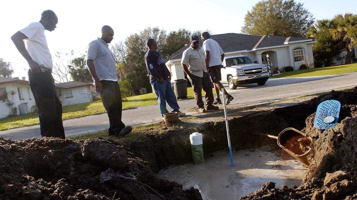 Tallevast residents look into a hole filled with dirty water which carried a definite odor. Just at the front edge of another nearby hole on 17th Street Ct. East is the top of a well used to test for contamination in the area in 2006.