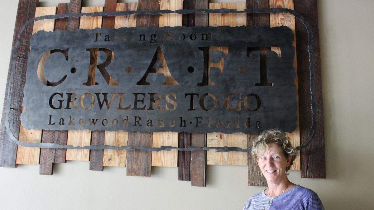 Jeanne Dooley is bringing Craft Growlers to Go and Tasting Room to Lakewood Ranch. She is shown with art work by Amy Jones commissioned for the new business. 
 JAMES A. JONES JR./Bradenton Herald