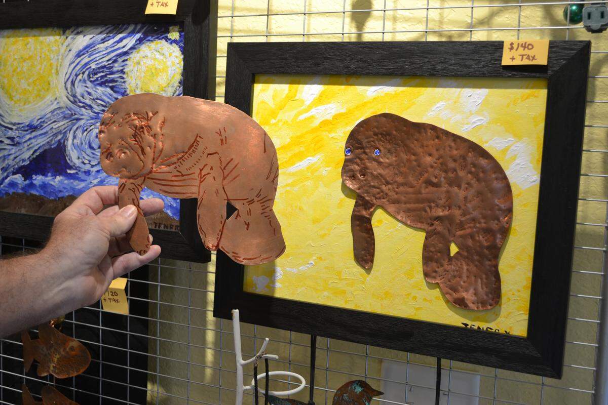 Village of the Arts resident artist Gene Tenery (14th Avenue West Studio) holds up a draft of Snooty the manatee in copper next to the final piece.
