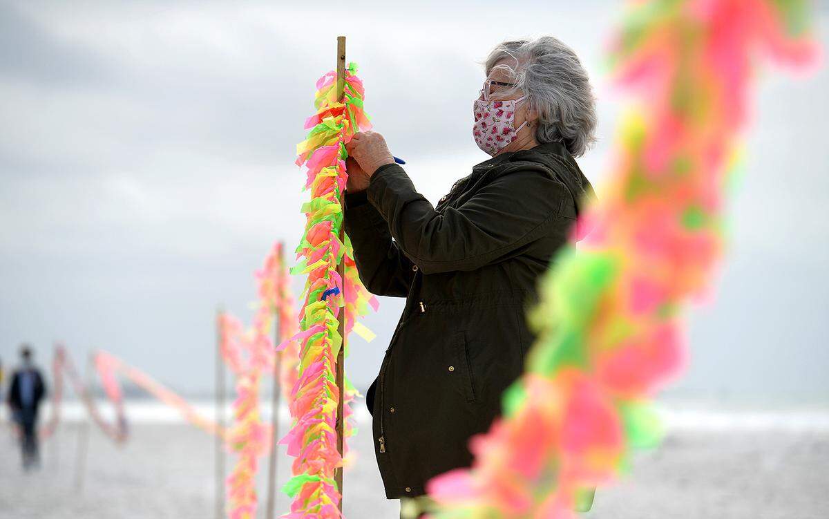 02/16/21--Ann Hoffman writes her brother’s name on a ribbon fluttering on a long garland with a group of people led by Cathy Tobias. They held a memorial created from ribbons and stretching 250 yards to remember the almost 27,000 people lost to COVID-19 in Florida.