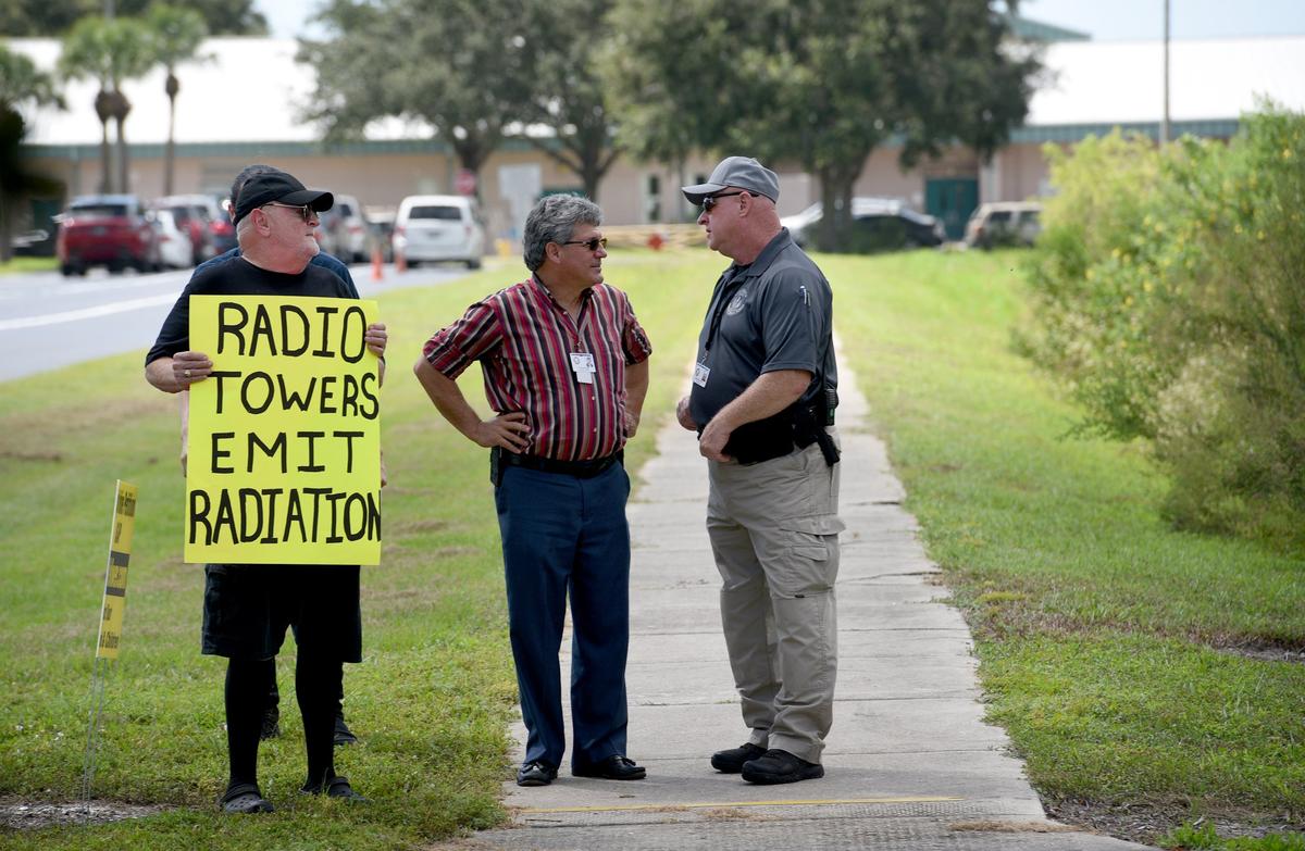 Scott Hopes, center, talks to school guardian as around 20 people stand outside Kinnan Elementary School at dismissal time Monday to hand out fliers and hold signs against the construction of a communications tower close by.