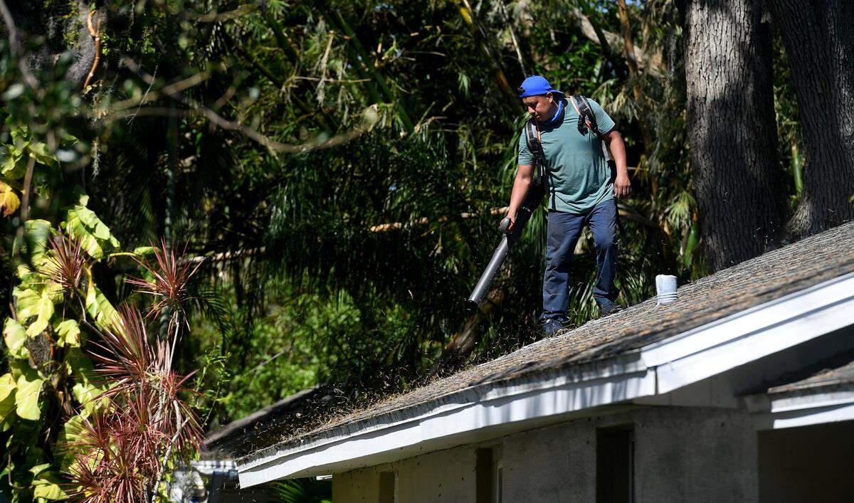 A man blows leaves from the roof of a house in East Bradenton as the county cleans up from the effects of Hurricane Ian on October 3, 2022.