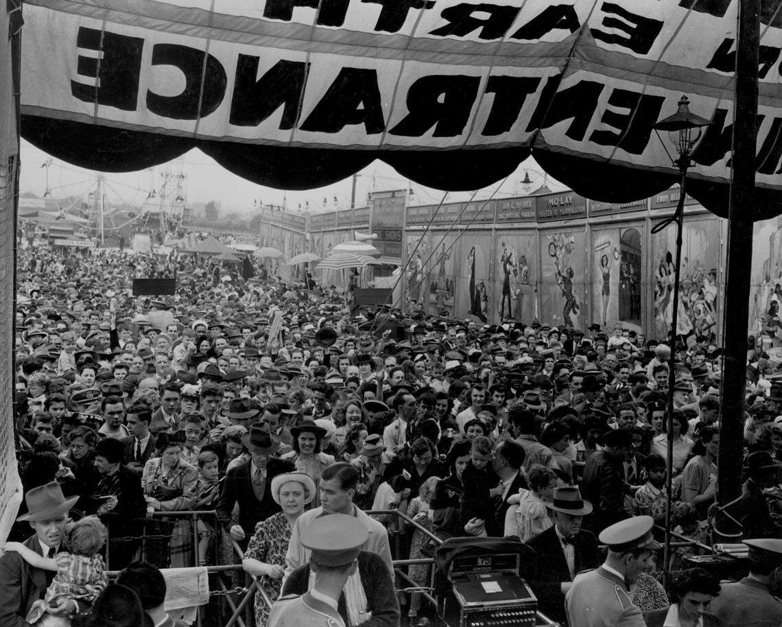 Crowds fill the main entrance of a venue to see the Ringling Bros./Barnum & Bailey Circus perform. Sideshow banners on the right advertise performers.