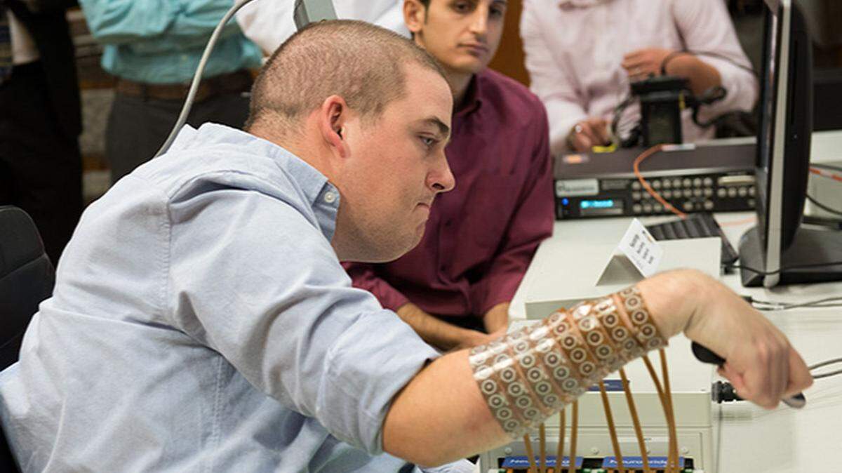 In this September 2014 photo provided by Ohio State University, Ian Burkhart participates in a study with neural bypass technology at The Ohio State University Wexner Medical Center in Columbus. A computer chip in Burkhart's brain reads his thoughts, decodes them, then sends signals to a sleeve on his arm, that allows him to move his hand. (Jo McCulty/Ohio State University Wexner Medical Center via AP)