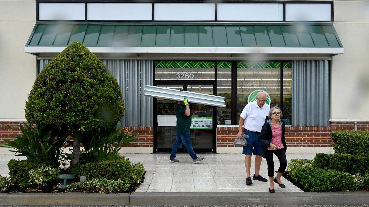 A Dollar Tree employee installs shutters while shoppers leave from making last minute purchases as Hurricane Idalia approaches on August 29, 2023.