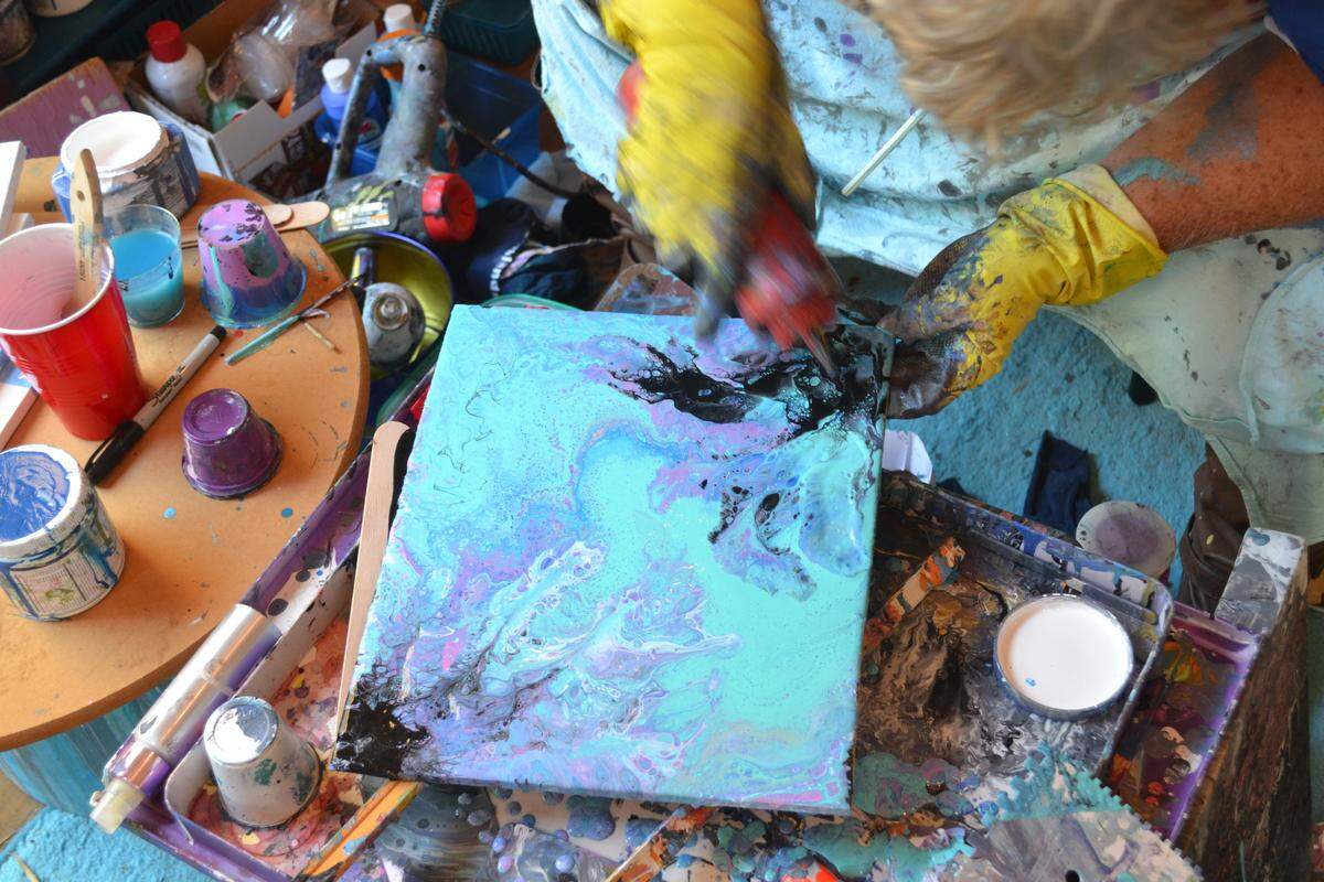 Cheryl Miller adds more paint to a work created using the “dirty pour” method of dumping layered paint onto a canvas.