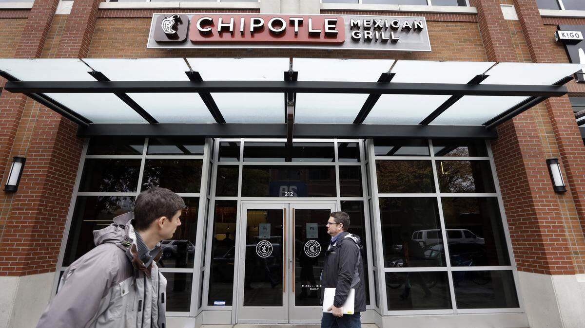 FILE - In this Nov. 9, 2015, file photo, pedestrians walk past a still-closed Chipotle restaurant in Seattle. An outbreak of E. coli that originated in the Pacific Northwest has spread south and east and has now infected people in six states. New cases have been reported in California, New York and Ohio, the Centers for Disease Control and Prevention said Friday, Nov. 20, 2015. (AP Photo/Elaine Thompson, File)