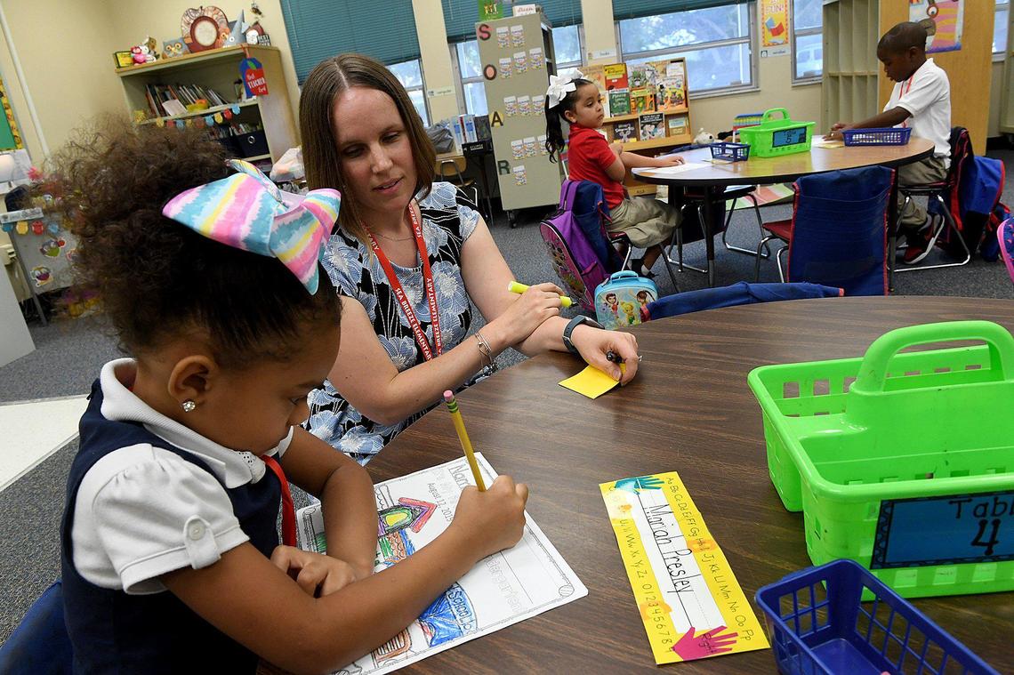 Seabreeze Elementary School kindergarten teacher Jennifer Minor watches as Mariah Presley writes her name on her paper on the first day of school for Manatee County students.