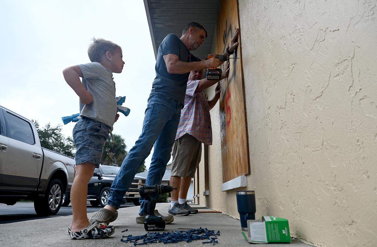 Branson Ellard, 4, Paul Connors, 59, and Gerald Grace help board up a friend’s West Bradenton business as Hurricane Milton approaches Manatee County on Oct. 7, 2024.