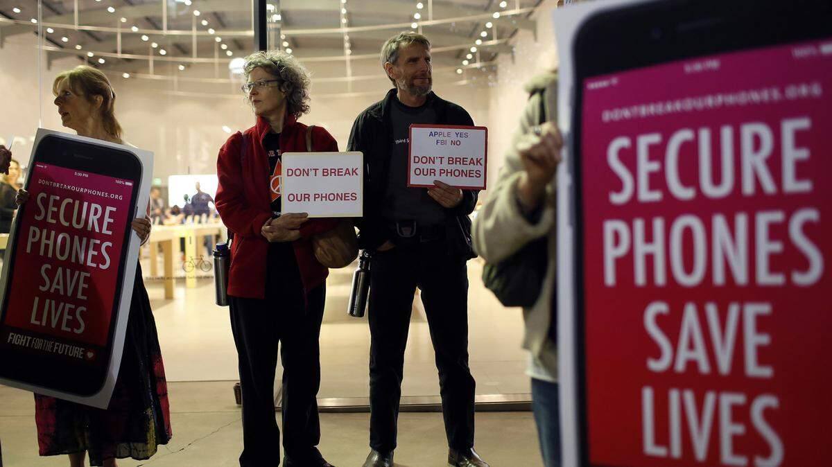 Protesters, from left, Sandra Bell, Victoria Best, and Charles Fredricks, hold signs in support of Apple store in Santa Monica, Calif., on Tuesday, Feb. 23, 2016. Rallies were planned at Apple stores across the country to support the company's refusal to help the FBI access the cell phone of a gunman who took part in the killings of 14 people at the Inland Regional Center in San Bernardino. (Katie Falkenberg/Los Angeles Times/TNS)