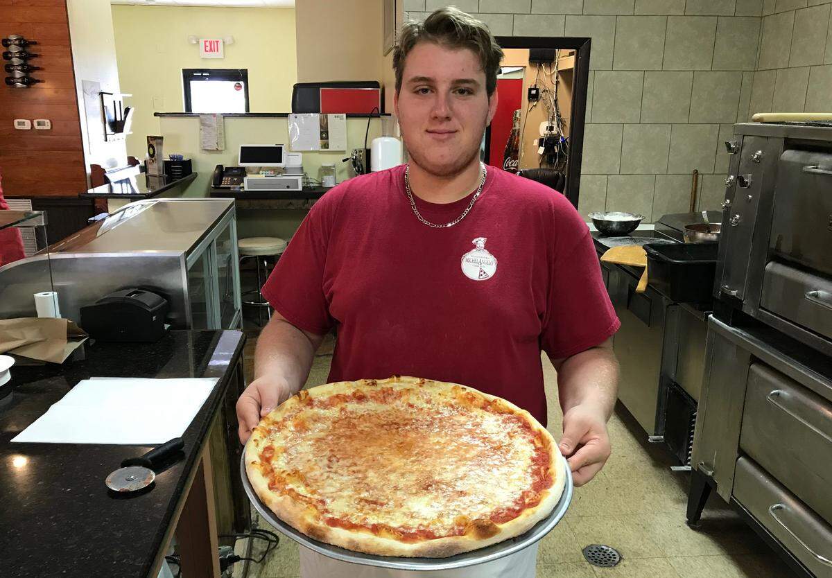 Pizza maker Matthew Metz holds a fresh-out-of-the-oven 16-inch cheese pizza at Lucca’s Pizza & Wine Bar, 817 14th St. W., Bradenton.