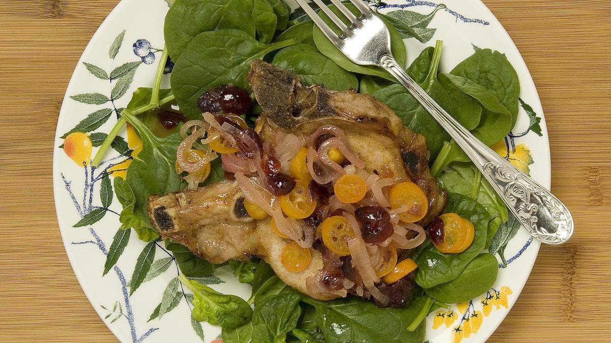 Pork chops with sweed-sour spicy Kumquat sauce is served over raw baby spinach leaves. (Nick Koon/Orange County Register/TNS)