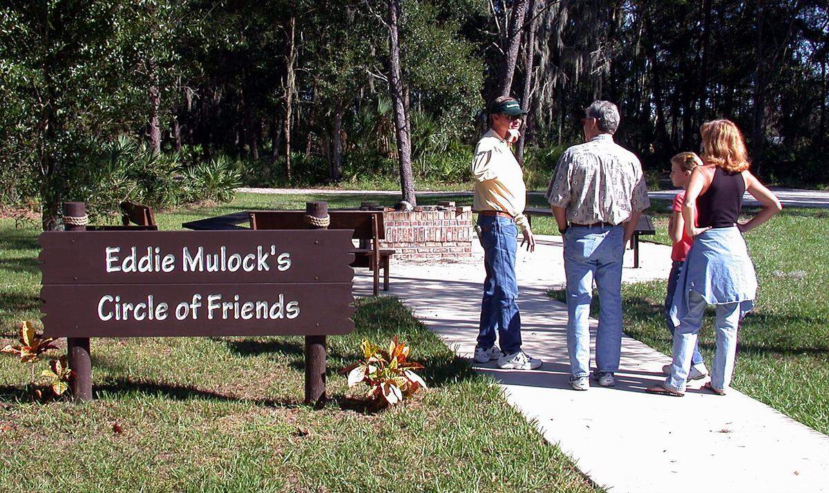 Bradenton attorney Eddie Mulock, left, founder of Foundation for Dreams, Inc. and Dream Oaks Camp, shows some visitors the camp fire site on Nov. 22, 2003. “When I created this camp, I always envisioned the kids sitting around the fire, and now that’s a reality here,” said Eddie. Members of the camp surprised him by labeling the camp fire site as Eddie Mulock’s Circle of Friends.