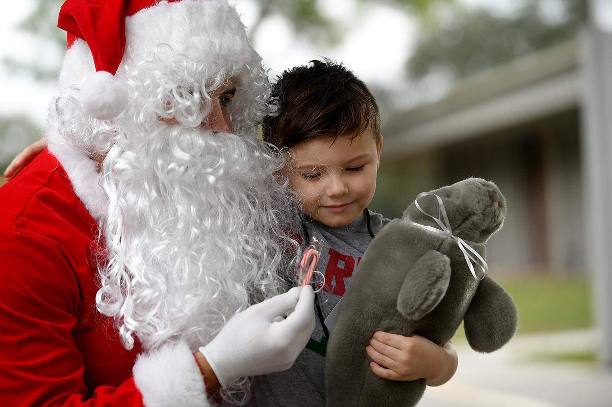 12/20/21—Christian Stefanoski hugs a plush manatee from Santa and eyes a sugar cane. Santa arrived on an East Manatee Fire Rescue truck to delight of pre-kindergarteners and ESE students at Bashaw Elementary School.