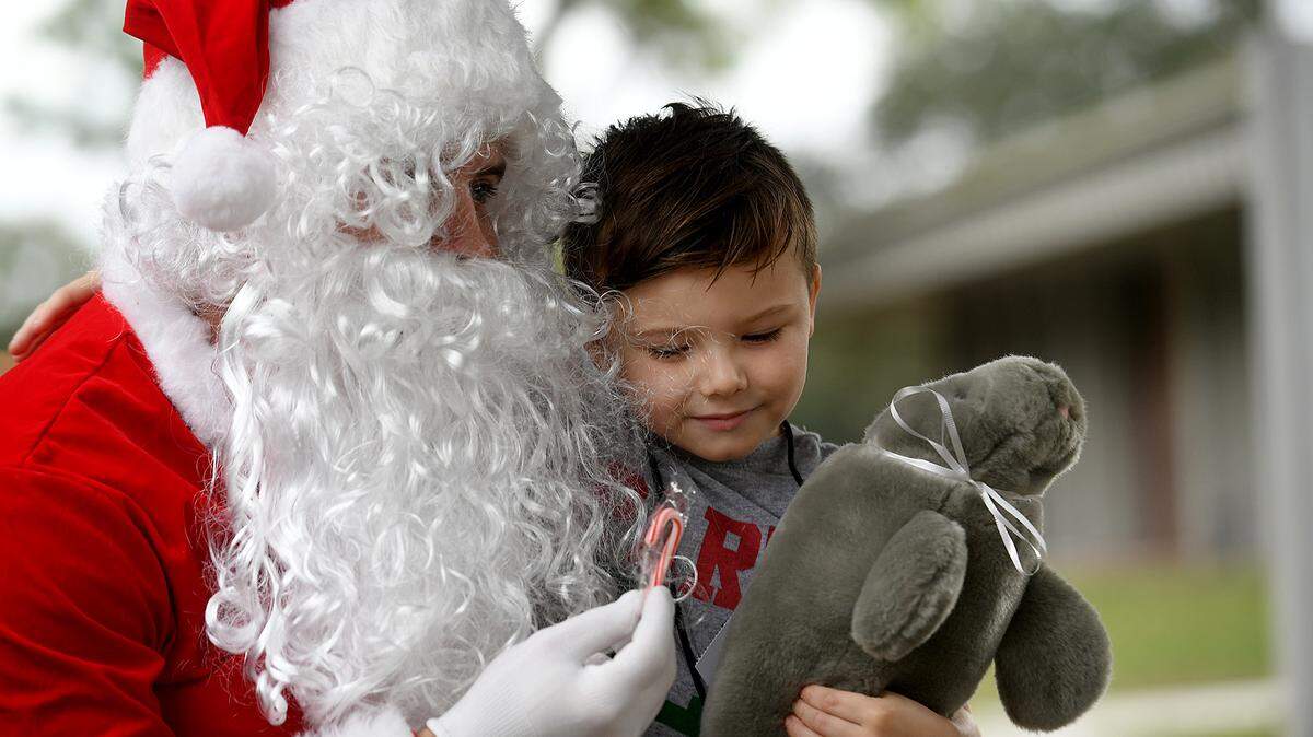 12/20/21—Christian Stefanoski hugs a plush manatee from Santa and eyes a sugar cane. Santa arrived on an East Manatee Fire Rescue truck to delight of pre-kindergarteners and ESE students at Bashaw Elementary School.