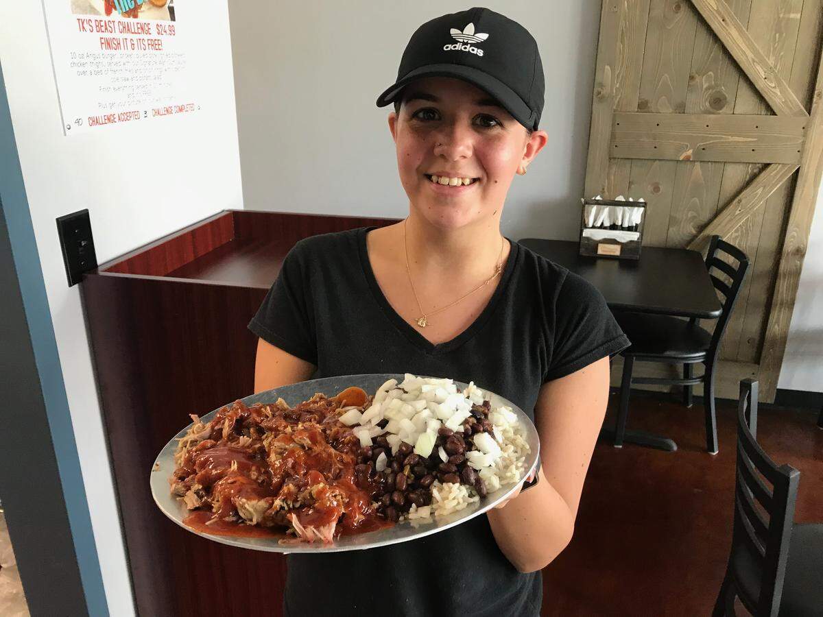 Emily Kohler serves the house special pulled pork platter with black beans and rice for $8.99 at TK Grill & Barbeque. The raw onions on top are optional.