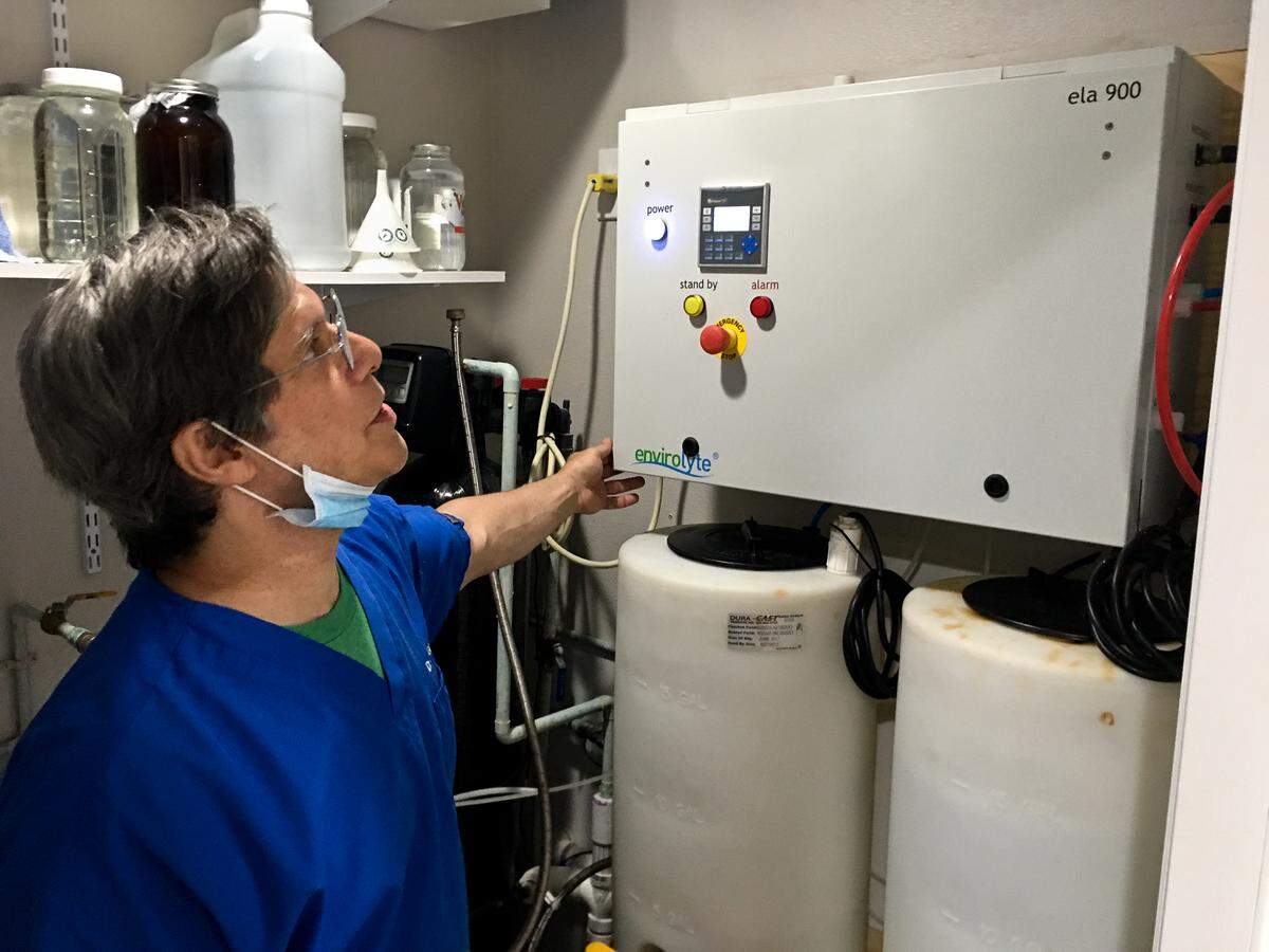 Ronald Gilbert, the owner of Gilbert Chiropractic Clinic, examines a machine that produces hypochlorous acid, the key ingredient in his sanitizer.
