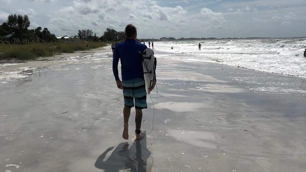 Surfer walks along an Anna Maria Island beach to take advantage of larger-than-usual waves caused by Hurricane Michael recently. The Manatee County Tourist Development Council is working to ensure that visitors return in force after red tide disappears from local waters.